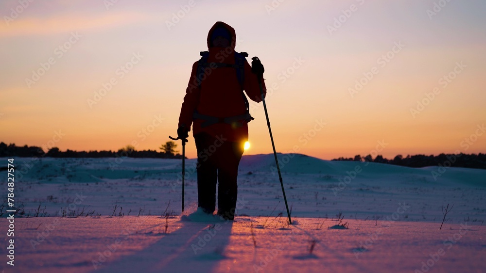 Tourist with backpack walks along snowy valley in rays of sunset to forest. Winter Expedition. Hike of successful backpacker heading for success and adventure. Vacation, healthy lifestyle, achieving