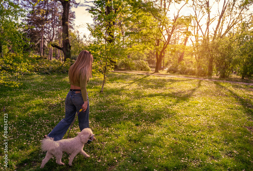 Pretty blonde walking her dog in the park, back view , idyllic sunset in background 