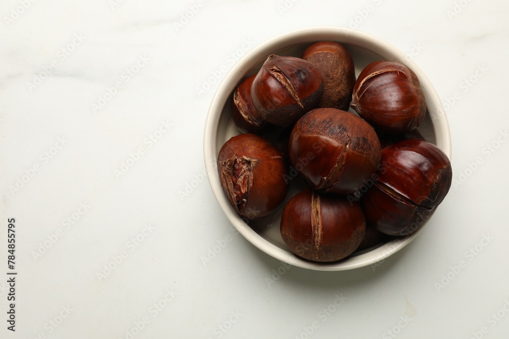 Obraz premium Roasted edible sweet chestnuts in bowl on white marble table, top view. Space for text