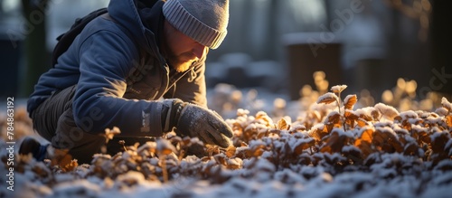 A young man in a blue jacket and gray knitted hat cleans the fallen leaves from the snow.