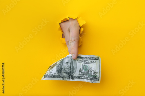 A right man's hand holds dirty money through a torn hole in yellow paper. Concept of dishonest income, donation, profit and salary fraud. photo