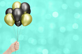 Female hand holds bunch of golden and black balloons on blurred green background. Empty space for text