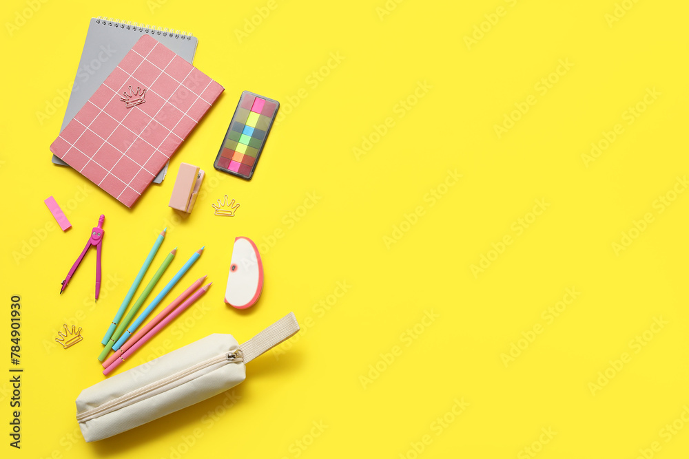 Beige pencil case with different school stationery and notebooks on yellow background Beige pencil case with different school stationery and notebooks on yellow background