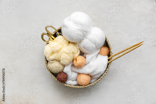 Basket with yarn balls, knitting needles and scissors on grey table