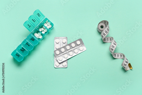 Container, blister packs with weight loss pills and measuring tape on turquoise background