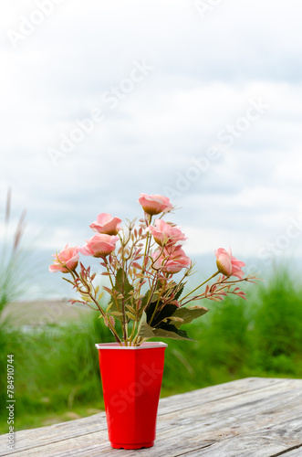 Pink rose flower in red vase on wooden table with nature background