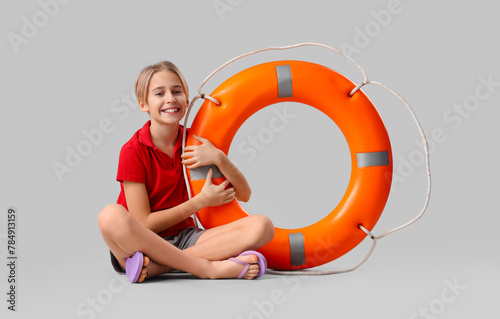 Happy little boy lifeguard with ring buoy sitting on grey background
