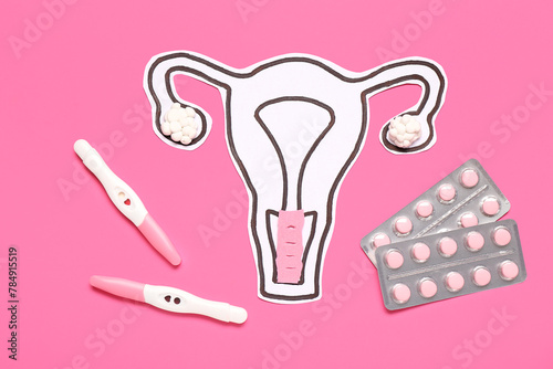 Paper uterus with pills and pregnancy tests on pink background
