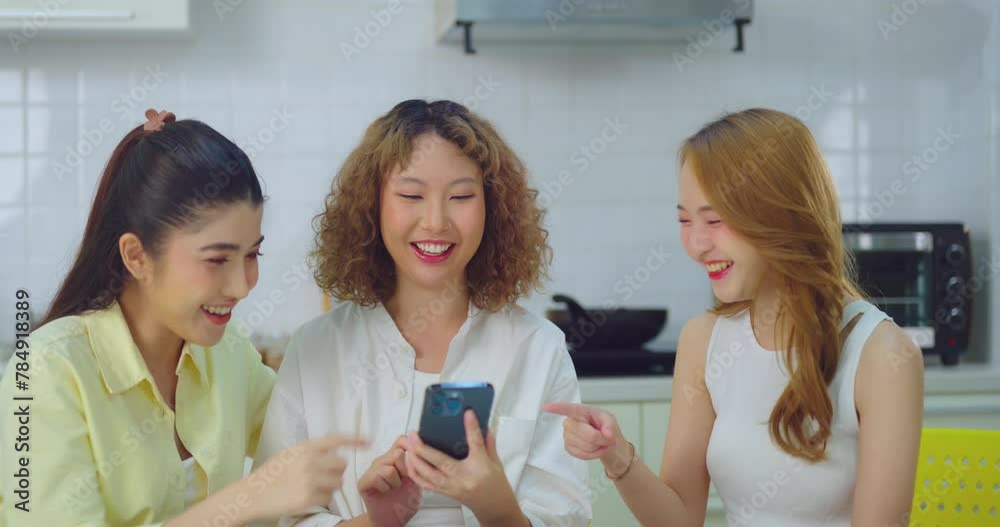 Group of three young women sharing a fun moment while looking at a smartphone in the kitchen. Group of three young women sharing a fun moment while looking at a smartphone in the kitchen.