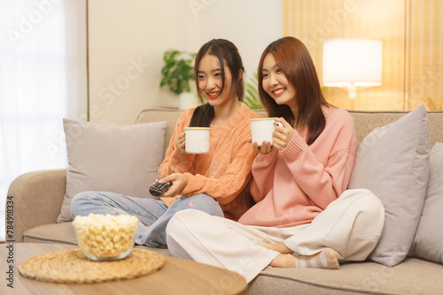 Friendship concept, LGBT lesbian couple drinking coffee and switching channel while watching movie
