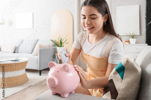 Female student putting money into piggy bank at home