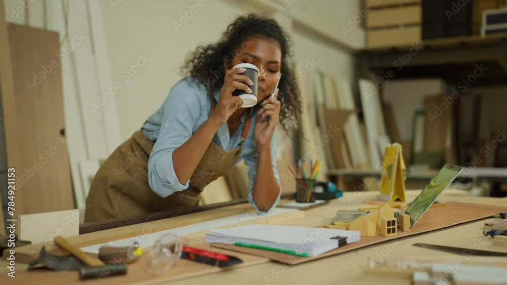 Professional carpenter or woodworker or charpentier woman drink coffee and call to customer during work with wood work product in workplace.