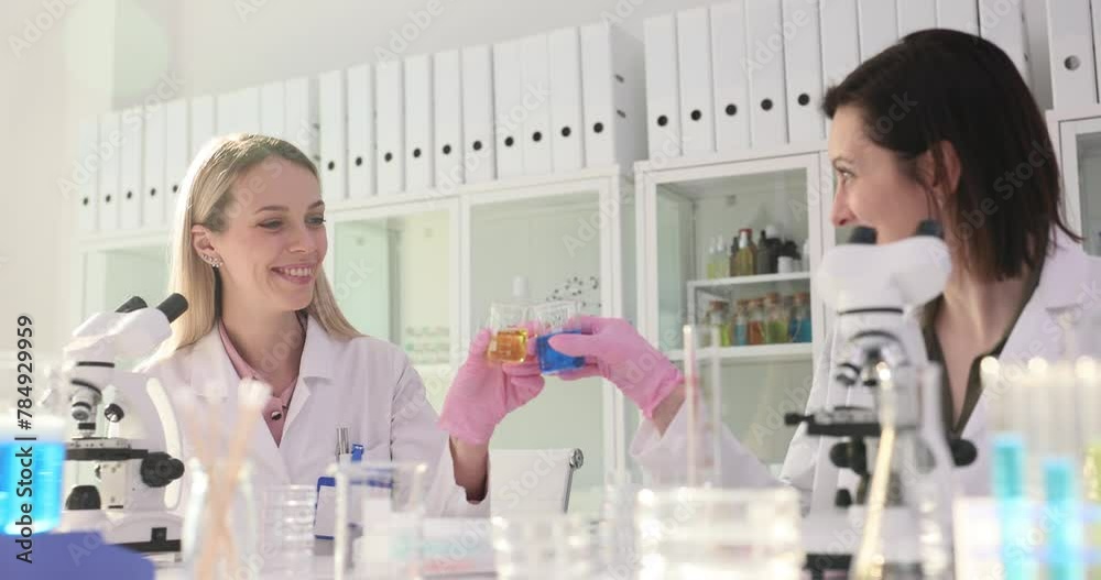 Two female scientists work in a laboratory and celebrate a successful chemical experiment by clinking glasses Two female scientists work in a laboratory and celebrate a successful chemical experiment by clinking glasses