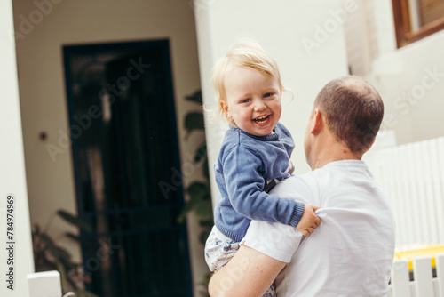 Toddler boy being held by his dad looking towards the camera giggling photo