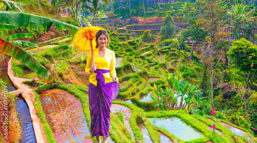 Portrait of balinese girl in traditional costume with yellow umbrella walking on rice terrace path - Terrace River Pool Swing in Ubud, Bali 