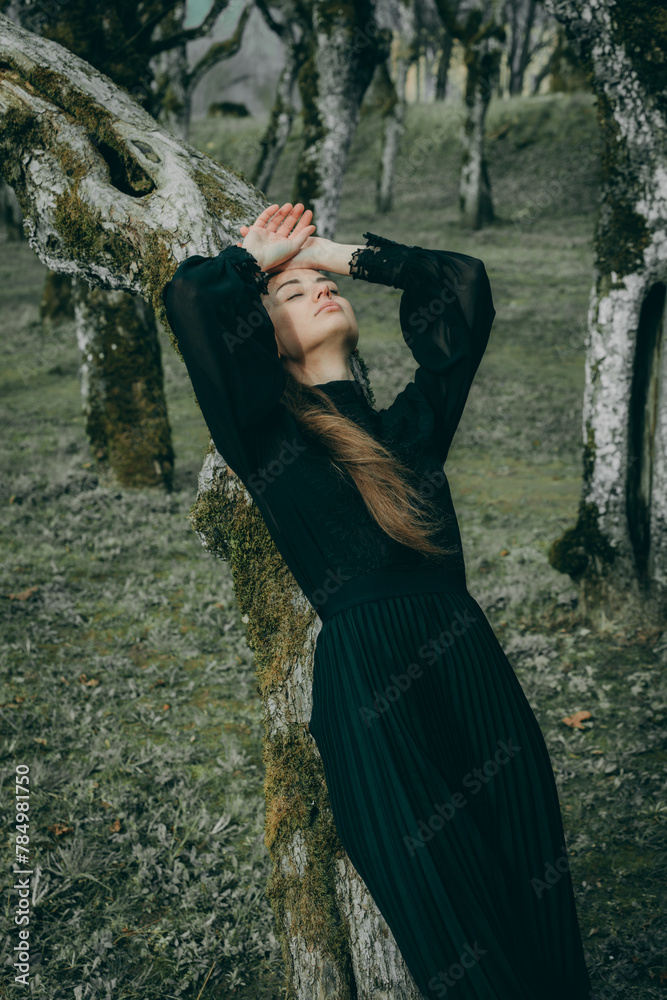 Woman in linden alley in dark clothes with long hair on blurred natural background