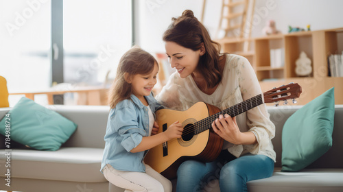 A young woman is teaching a girl to play guitar in living room. Mom and Daughter, mother's day, children's day