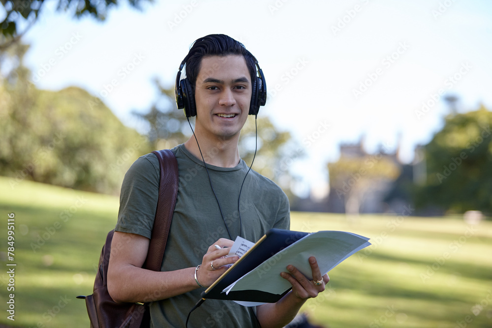 Young man with dark hair outside holding device wearing headphones at park Young man with dark hair outside holding device wearing headphones at park