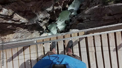 Man explores standing on top of bridge with metal railing and tall drop off to see downcut valley photo