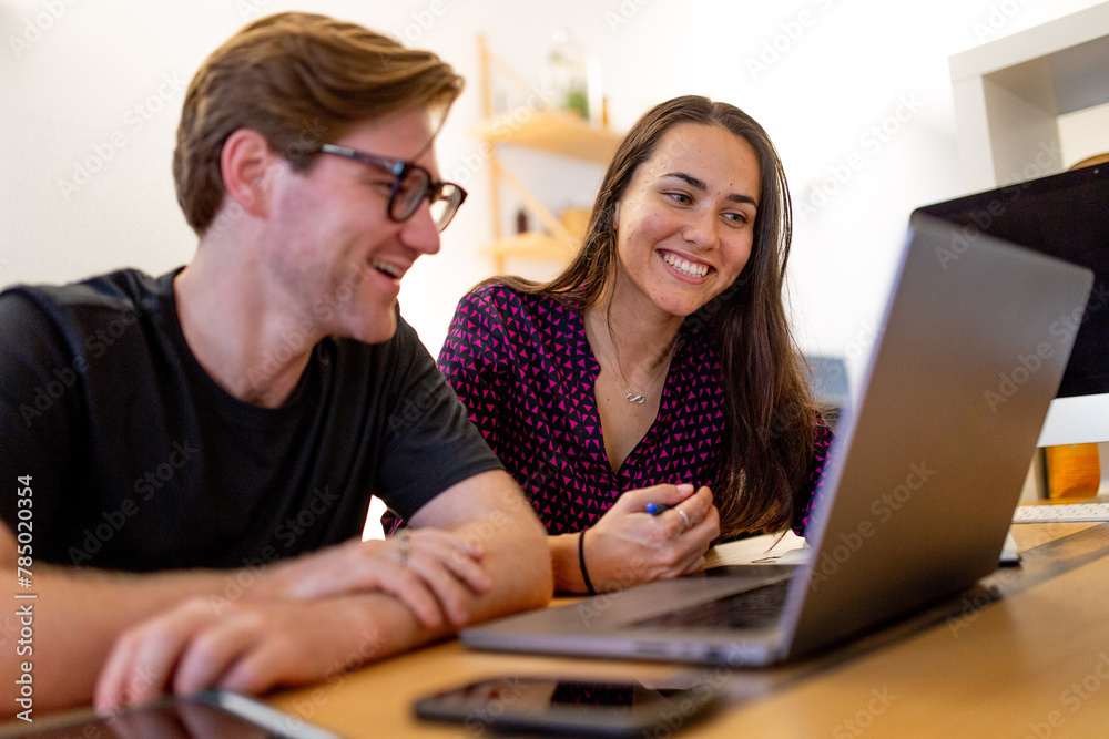 Caucasian man and Aboriginal woman sitting together at a table in an office looking at a laptop Caucasian man and Aboriginal woman sitting together at a table in an office looking at a laptop