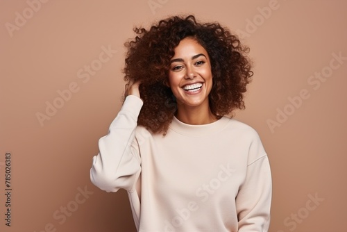 A woman with curly hair is smiling and wearing a white sweater