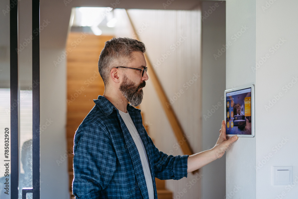 Fototapeta premium Smart home system. Man adjusting household functions, lighting, security cameras, door locks and smart thermostat or heating settings. Concept of sustainable and smart technology at home.