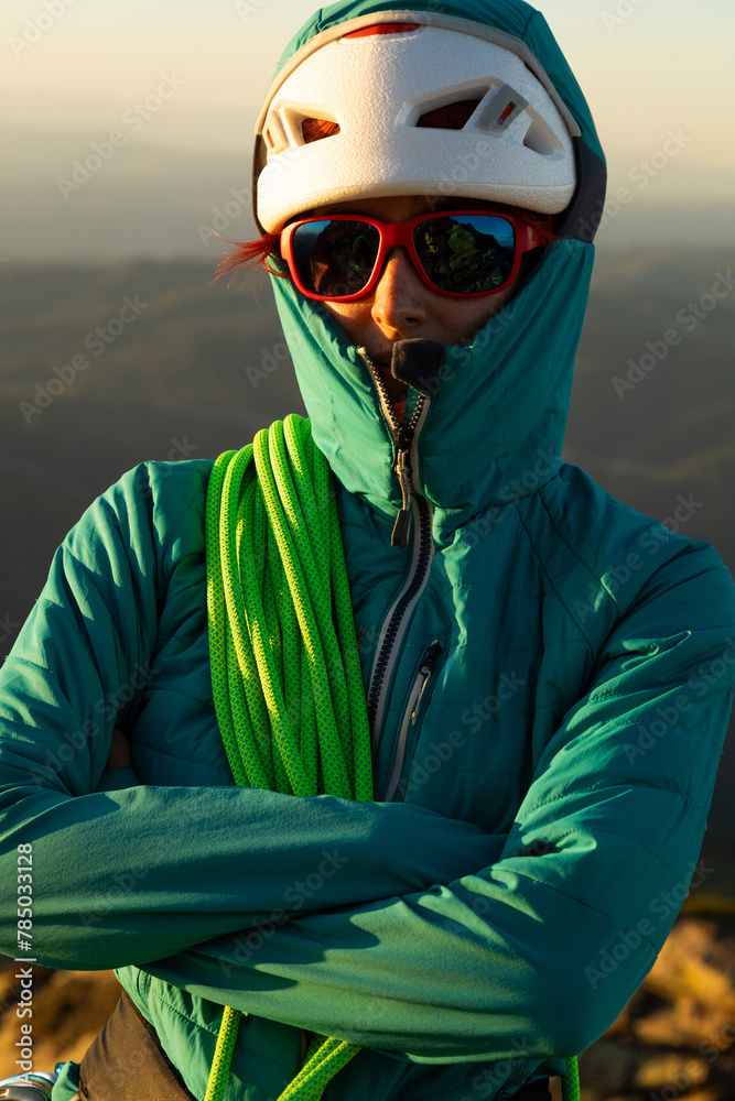A woman in a green jacket with a red helmet and goggles. She is holding a green rope A woman in a green jacket with a red helmet and goggles. She is holding a green rope