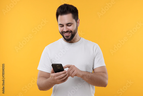 Happy young man using smartphone on yellow background © New Africa