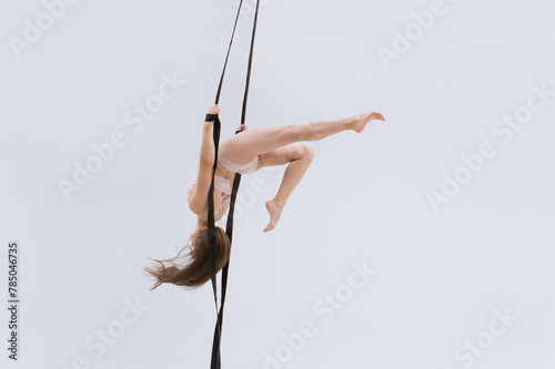 Horizontal photo of a Flexible aerial gymnast performing using gymnast slings. Flying in the air. Gymnast stunt. Professional athlete.