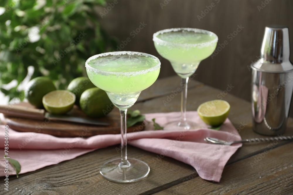 Delicious Margarita cocktail in glasses, lime and shaker on wooden table, closeup