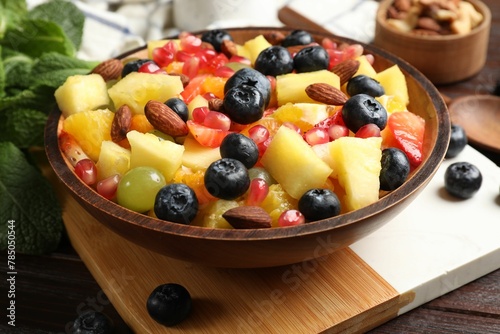 Delicious fruit salad in bowl  berries  nuts and fresh mint on wooden table
