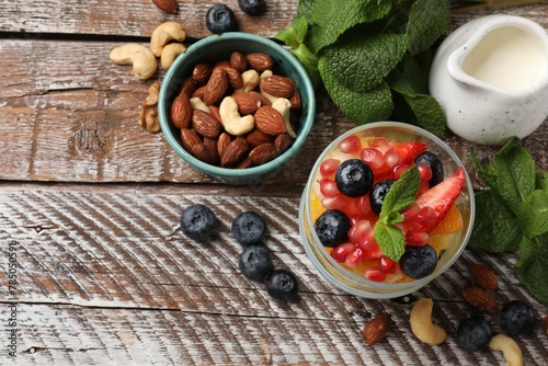 Delicious fruit salad, fresh berries, mint and nuts on wooden table, flat lay. Space for text
