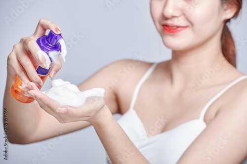 Female hands using cosmetic liquid soap or hand sanitizer close up. Cosmetics foam pump container, facewash dispenser in a woman's hand. Smiling young woman washing foam face by natural foamy gel.