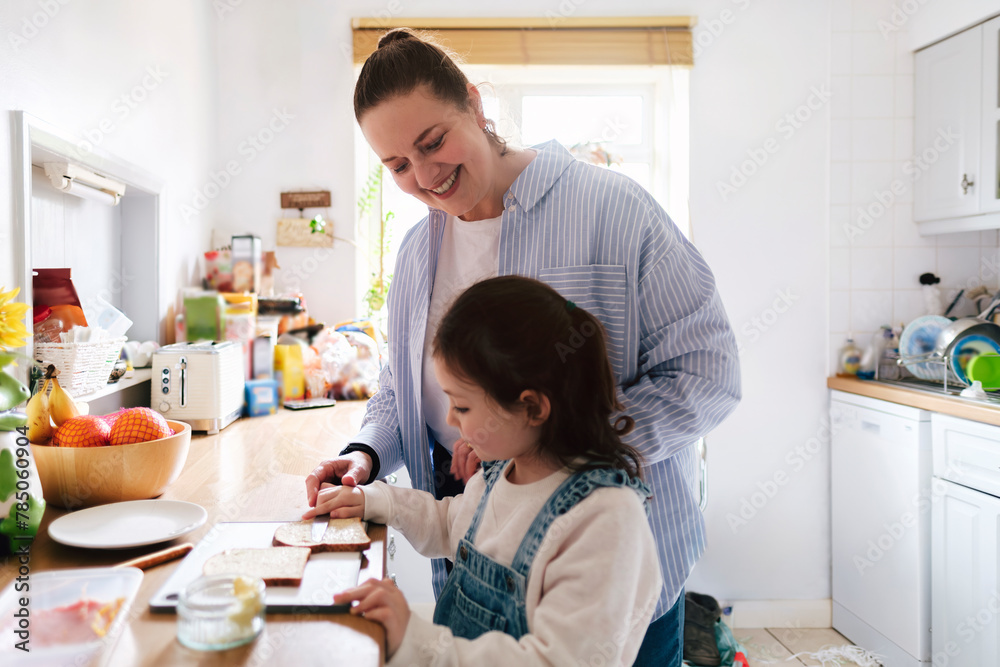 Happy mother with daughter applying butter on bread at home Happy mother with daughter applying butter on bread at home