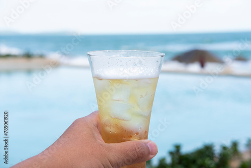 hand holding glass of lager beer on pool beach and sea background