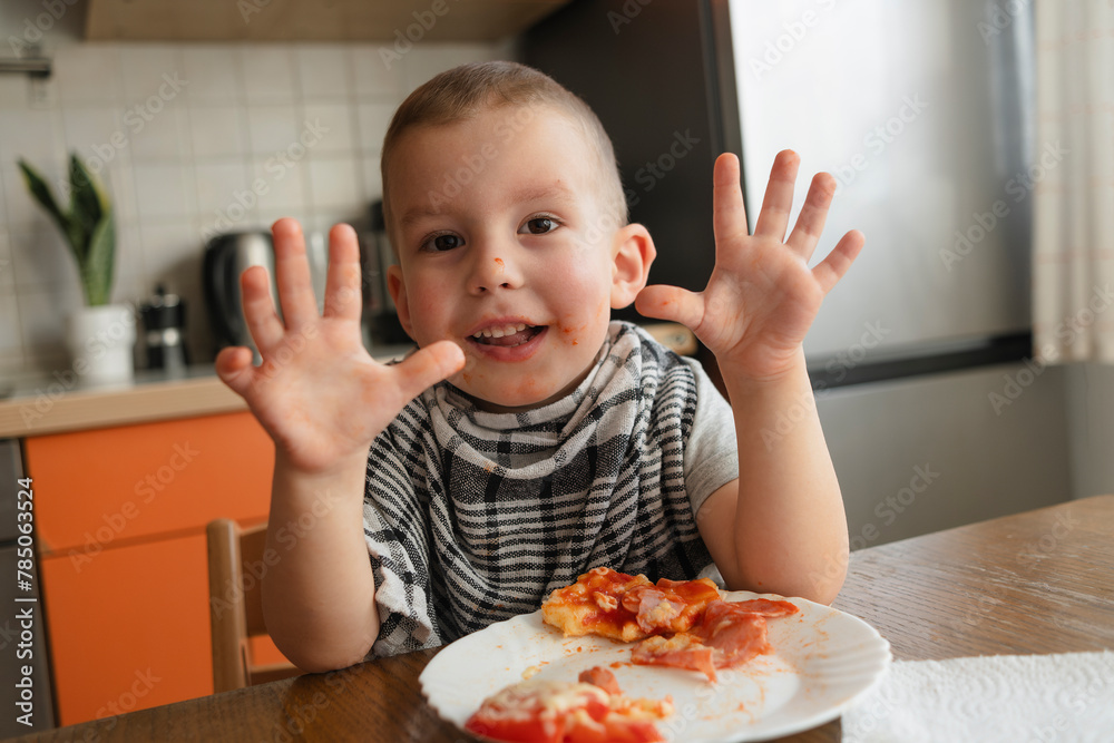Happy boy showing hands near pizza at table in kitchen Happy boy showing hands near pizza at table in kitchen