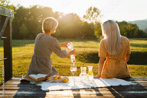 Woman pouring juice by friend and having picnic in park photo