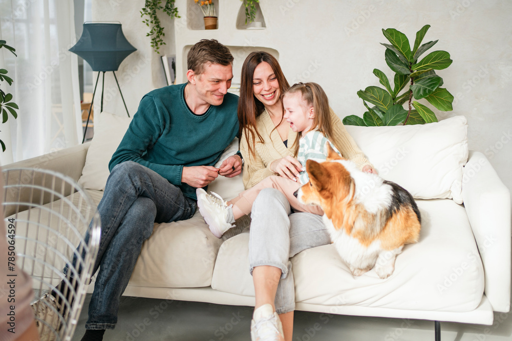 Happy family sitting with daughter and pet dog on sofa at home Happy family sitting with daughter and pet dog on sofa at home