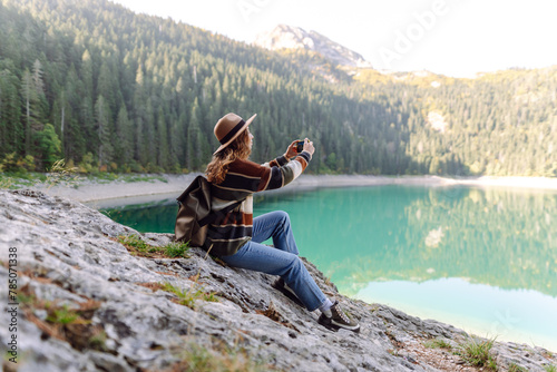Woman using her phone for video call on the mountain. Selfie time. Enjoying nature alone and taking picture on smartphone. Lifestyle, adventure, nature.