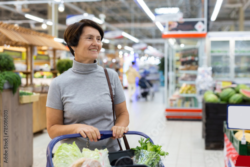 Mature woman standing in grocery store with groceries in cart