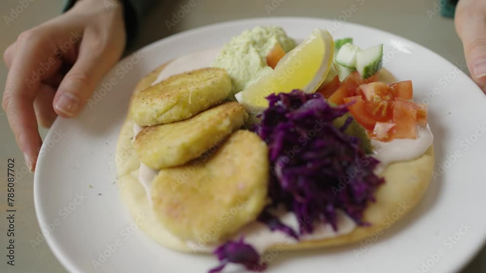 Vegan falafel cutlets with pita and vegetables on a plate. Close-up of a plate filled with golden fried patties, creamy hummus, crisp vegetables, and vibrant red cabbage, ready to be savored. Vegan falafel cutlets with pita and vegetables on a plate. Close-up of a plate filled with golden fried patties, creamy hummus, crisp vegetables, and vibrant red cabbage, ready to be savored.