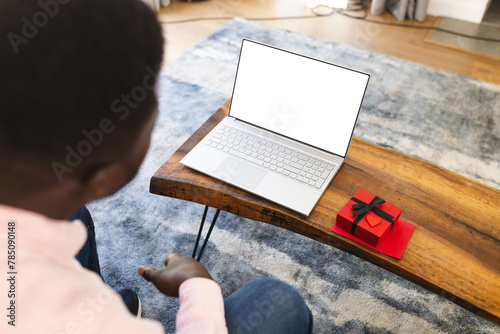 African American man on a video call with gift, looking at laptop with copy space