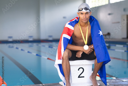 Male athlete swimmer wrapped in Australian flag sitting on podium with gold medal