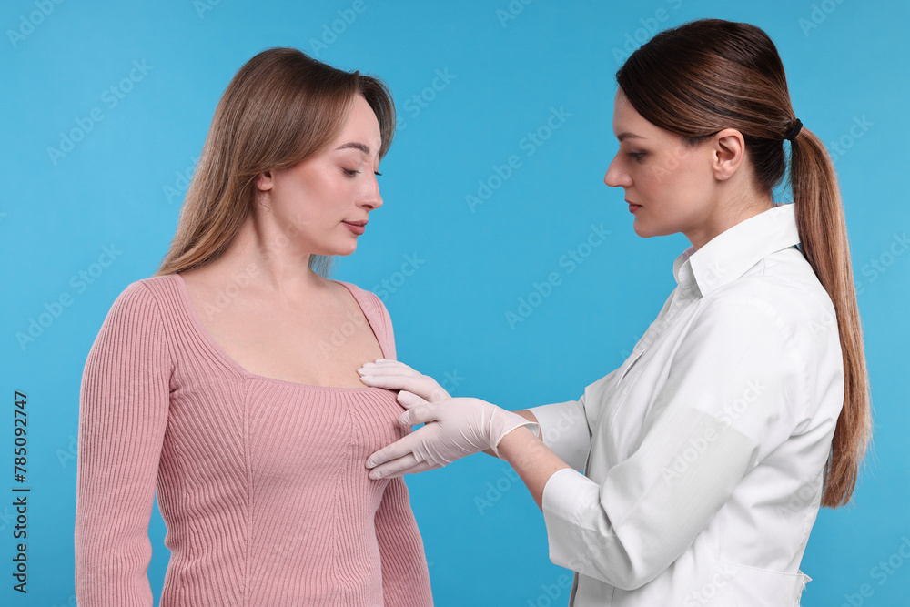 Mammologist checking woman's breast on light blue background