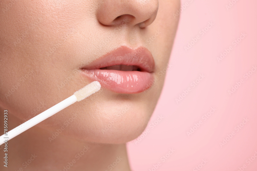 Woman applying lip gloss on pink background, closeup. Space for text