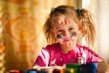 A girl with paints, her face painted in bright colors, her expression full of delight and joy.