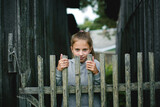 A teenage girl by a wooden fence, her face expressing quiet determination and tenderness.