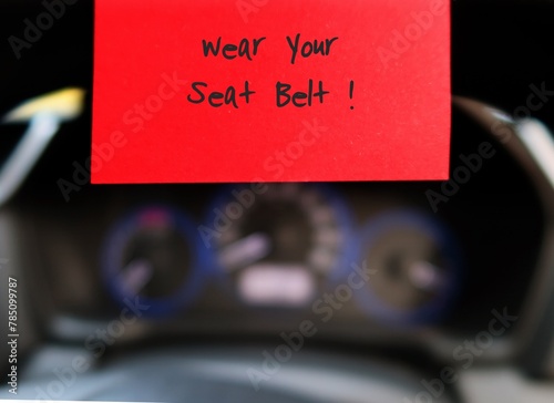 Red sticky note with text written WEAR YOUR SEAT BELT  on the car steering wheel , to remind driver to wear safety bealt before driving .