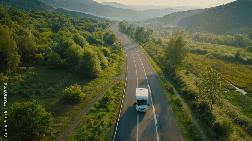 Motorhome traveling along an empty road in the lush green mountain valley, aerial view
