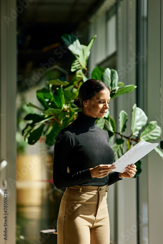 An elegant businesswoman reading one document, standing by the window on a sunny day.